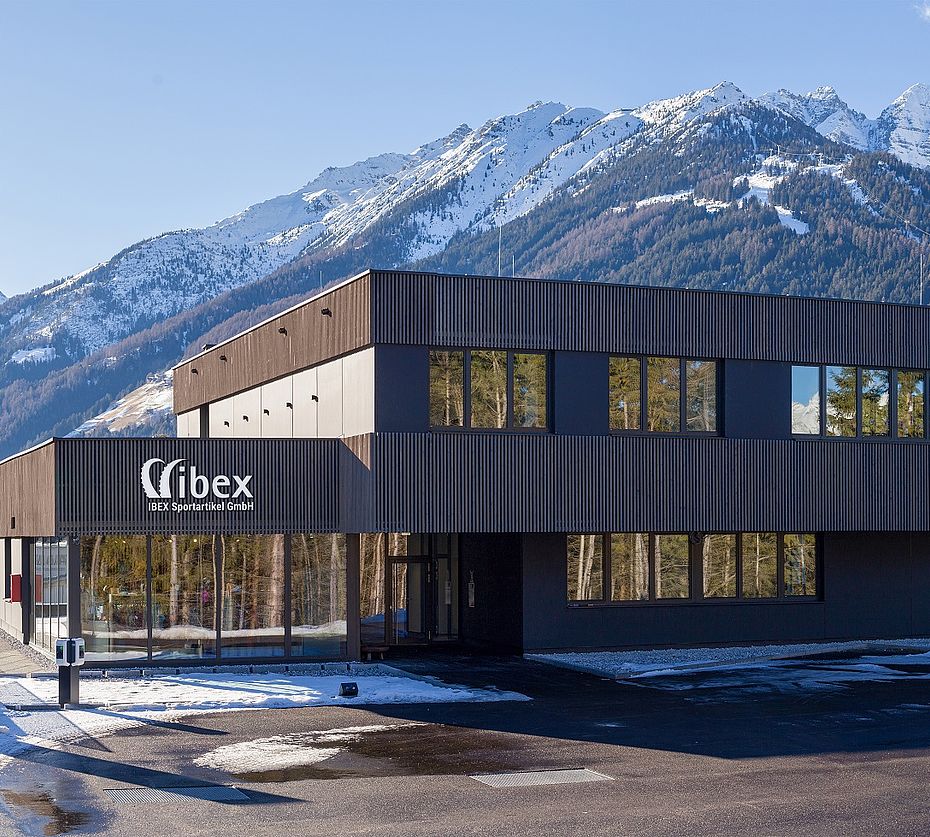 IBEX Sportartikel Firmengebäude mit dunkler Fassade vor schneebedeckten Alpen